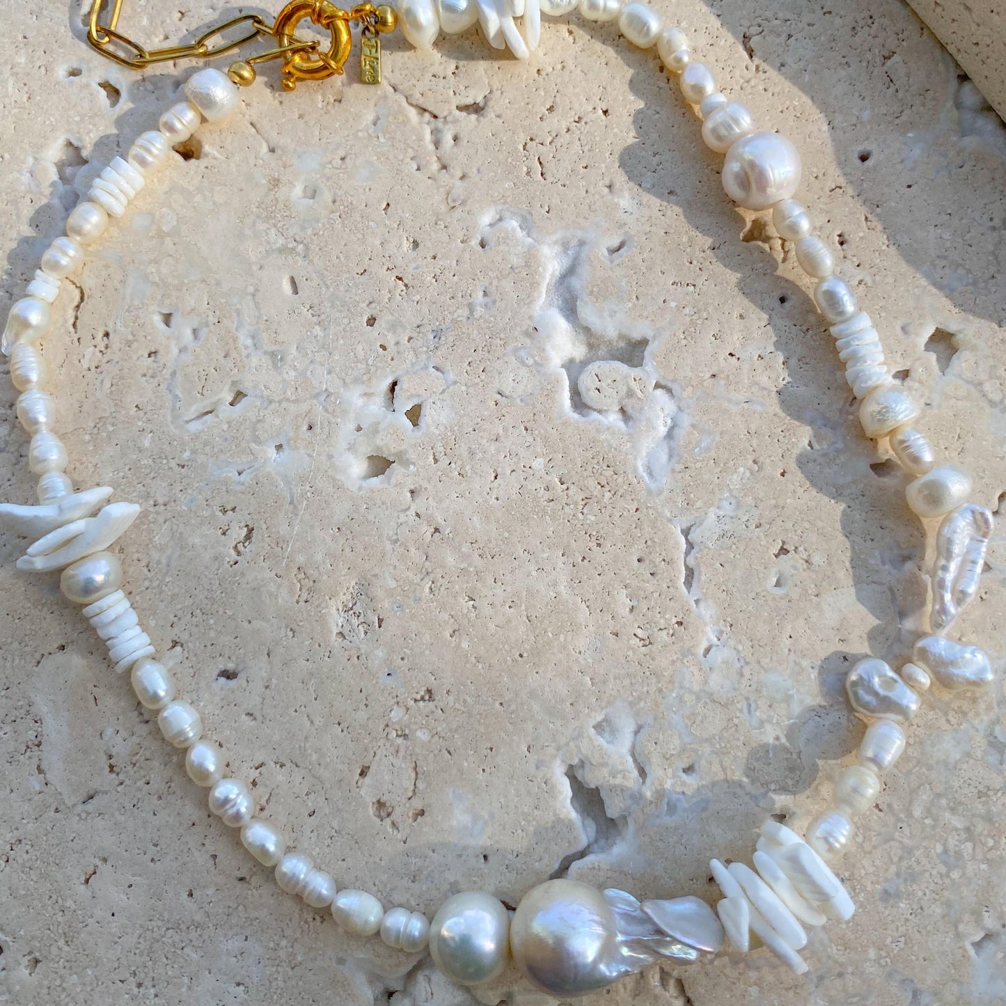A white choker necklace with gold accents and pearl beads, displayed against a textured background.
