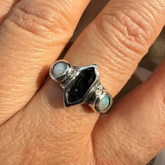 A close-up of a hand wearing a silver ring with a central black stone and two light blue-green stone accents.