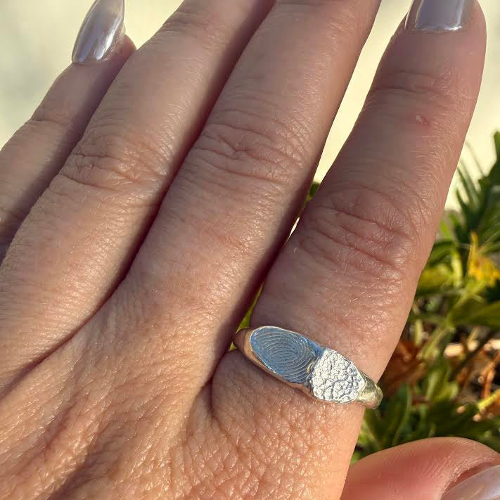 A close-up of a hand wearing a silver ring with a split design: fingerprint ring