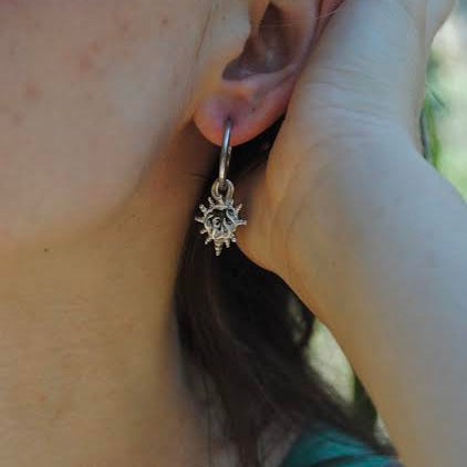 Close-up of an ear with a heart-shaped earring, held by a hand.