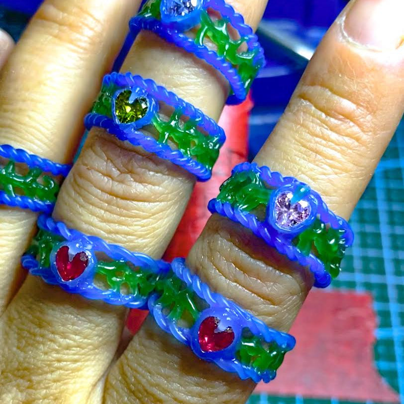 Fingers wearing colorful plastic rings with gemstones on a cutting mat background