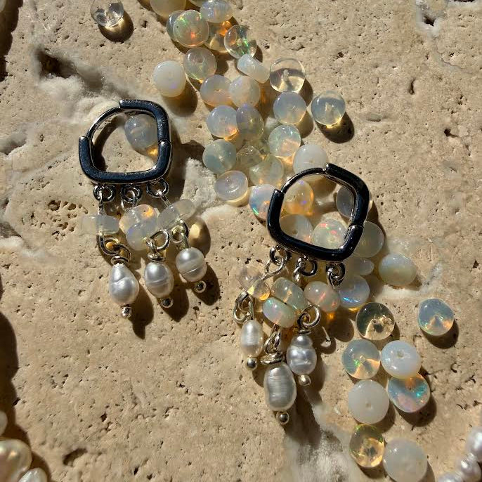 Pair of earrings with black square tops and pearl-like beads on a textured surface