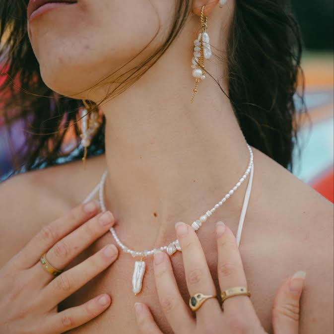Close-up of a woman wearing a pearl necklace with her hands on her chest.