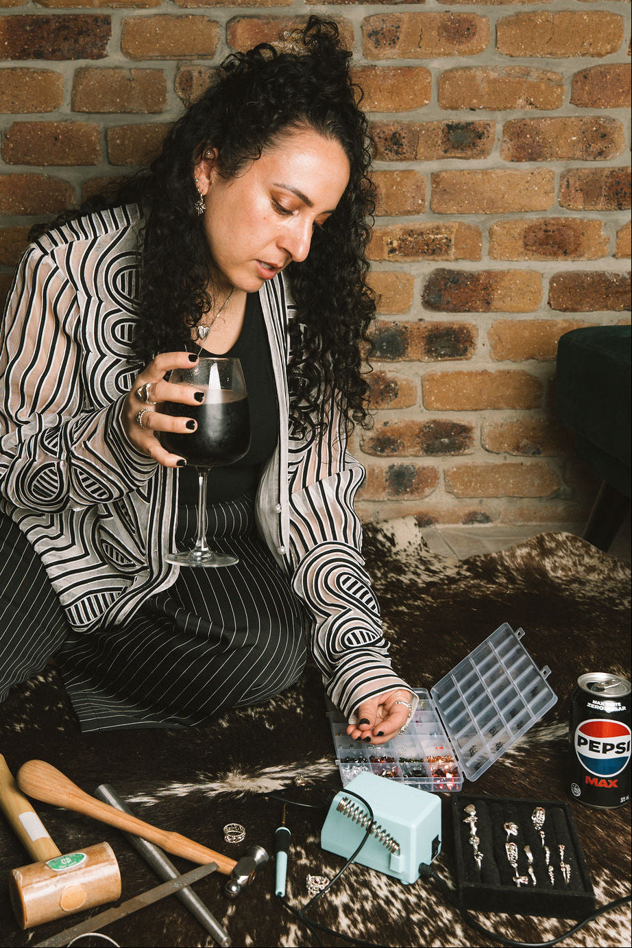Woman sitting on a couch with a glass of pepsi max, surrounded by various items including a bottle opener and a can of Pepsi, against a brick wall.