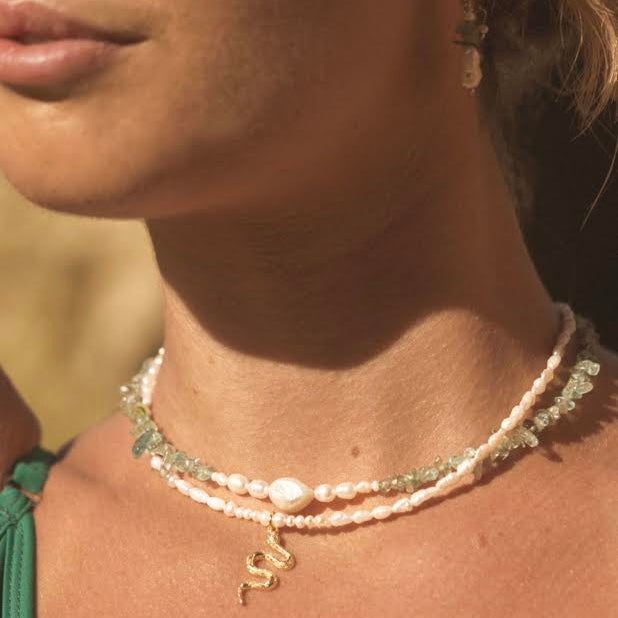 Close-up of a person wearing multiple necklaces with a blurred natural background