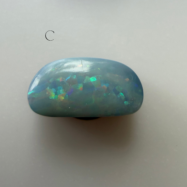A polished blue opal stone with iridescent flashes of green, orange, and purple, photographed on a plain light background.