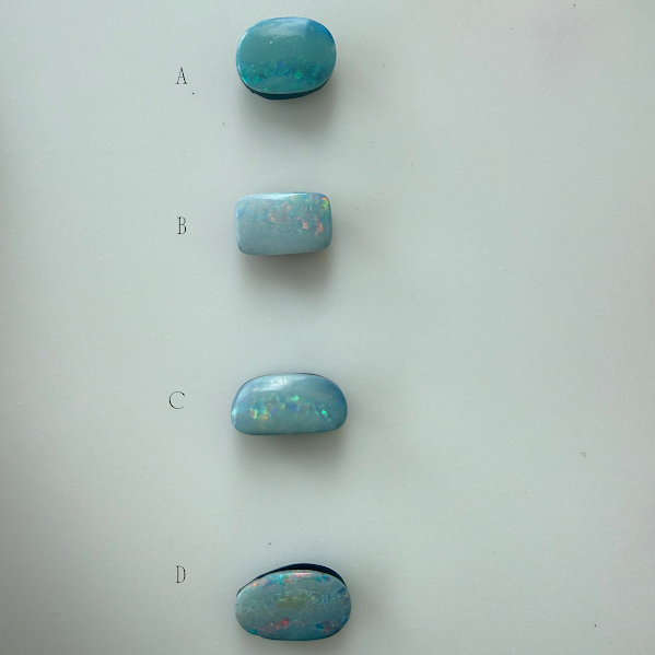 Four oval cabochon doublet opals gemstones in shades of light blue and turquoise with opalescent play-of-color, labeled A, B, C, and D on a plain light background.