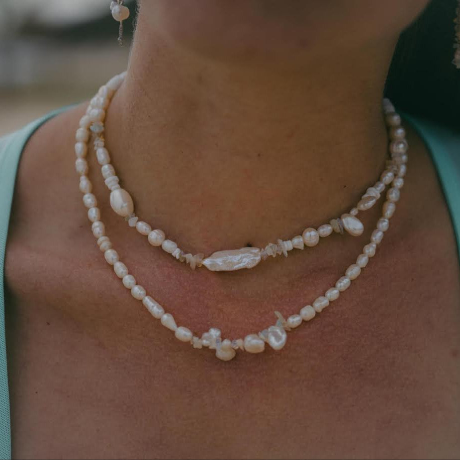 Close-up of a person wearing a pearl necklace and earrings with a blurred background