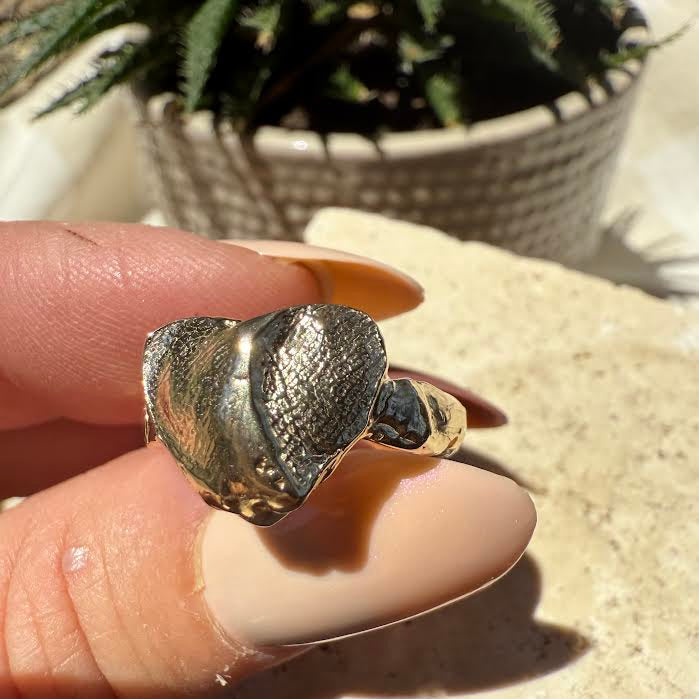 solid gold ring with a textured design held between fingers against a natural background