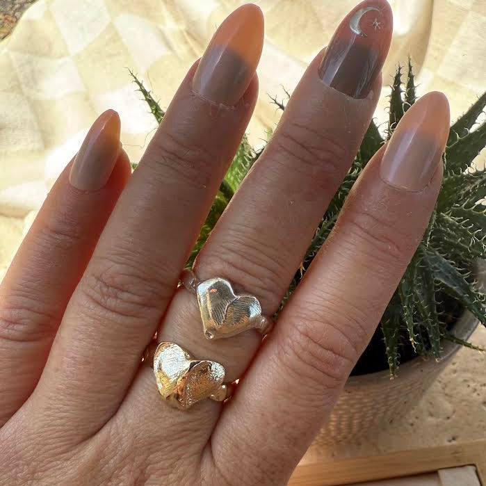 Hand wearing two gold heart-shaped rings with a blurred background
