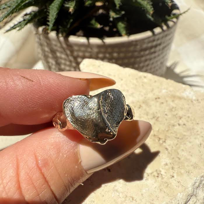 Heart-shaped fingerprint solid gold ring held between fingers with a natural background