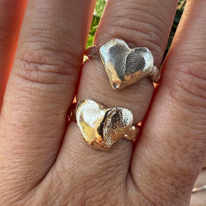 Two heart-shaped gold rings on a person's finger with a blurred natural background.
