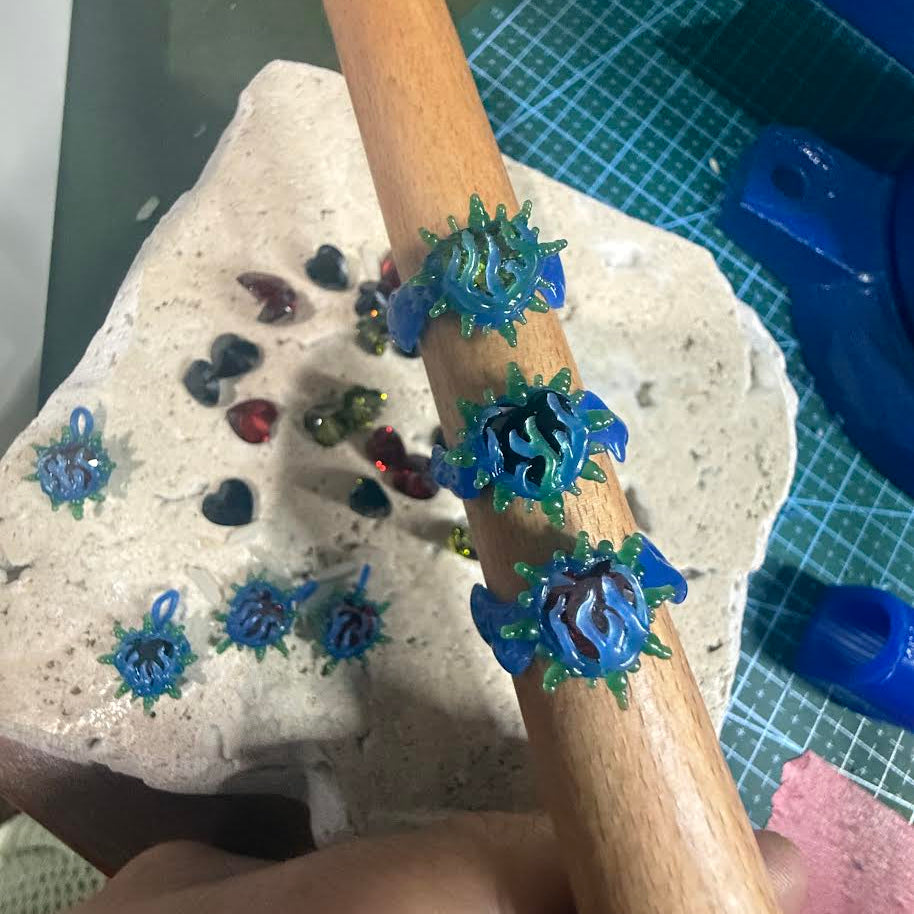 Decorative blue flower embellishments on a wooden stick with a stone and small stones in the background.
