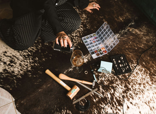 Person sitting on a cowhide rug with jewelry-making supplies including beads, tools, and a glass of pepsi max.
