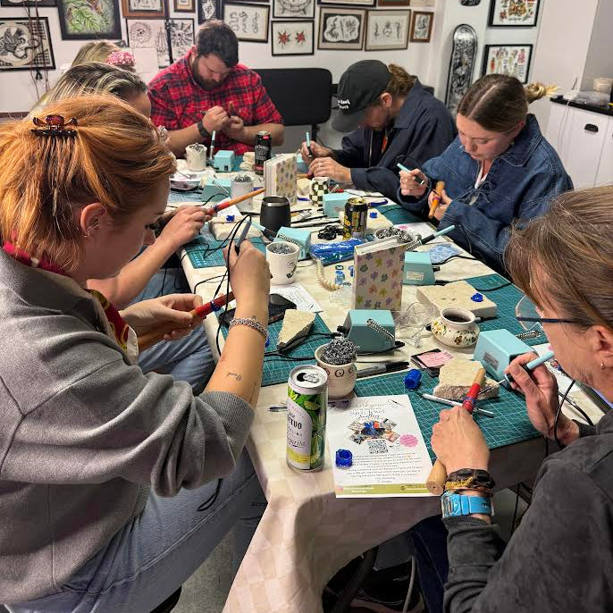 Group of people sitting around a table in a tattoo studio with various tattoo designs on the walls.
