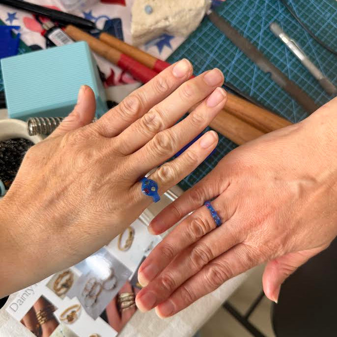 Two hands with blue rings on a crafting table with tools and materials. lostwax rings