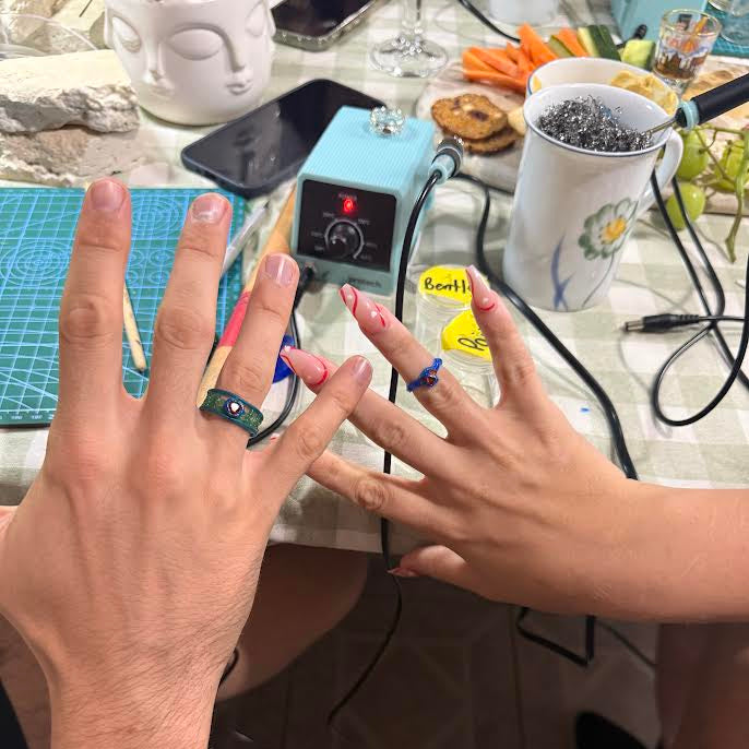 Close-up of two hands with nail art designs on a table with various items.