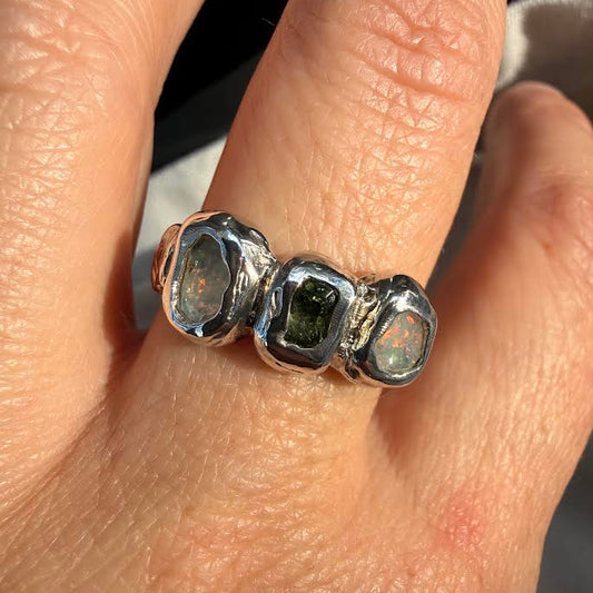 A close-up of a hand wearing a chunky sterling silver ring with three faceted, bezel-set iridescent stones.