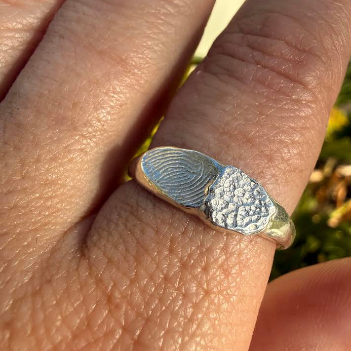 A sterling silver ring with a fingerprint and textured cluster design, shown worn on a person's finger in an outdoor setting.