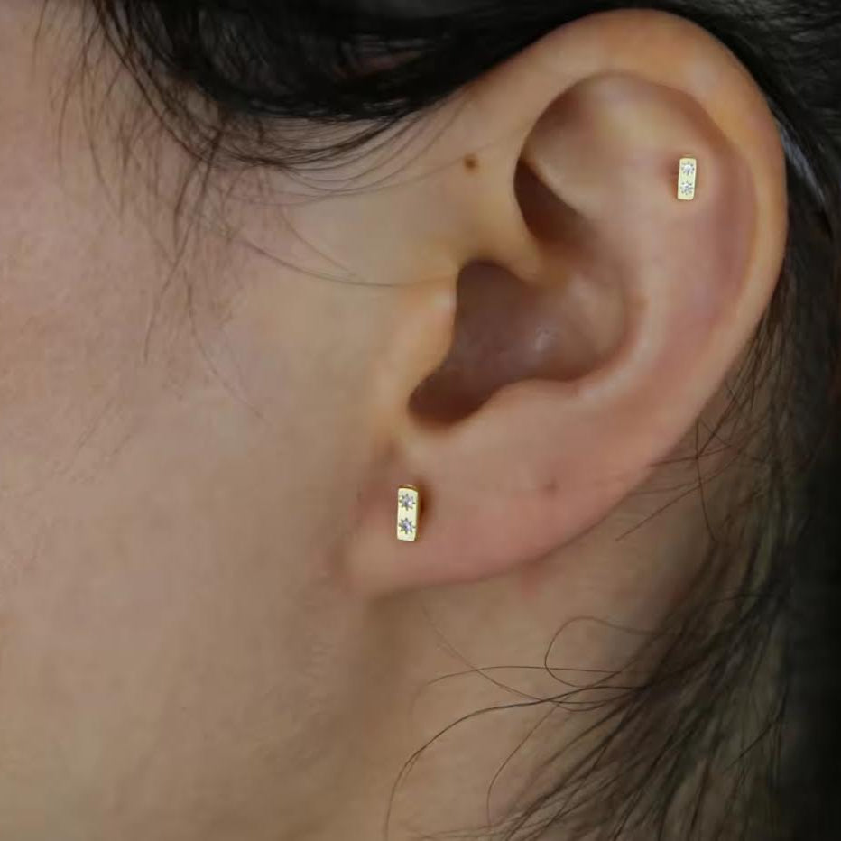 Close-up of an ear wearing gold  stud earrings with a blurred background